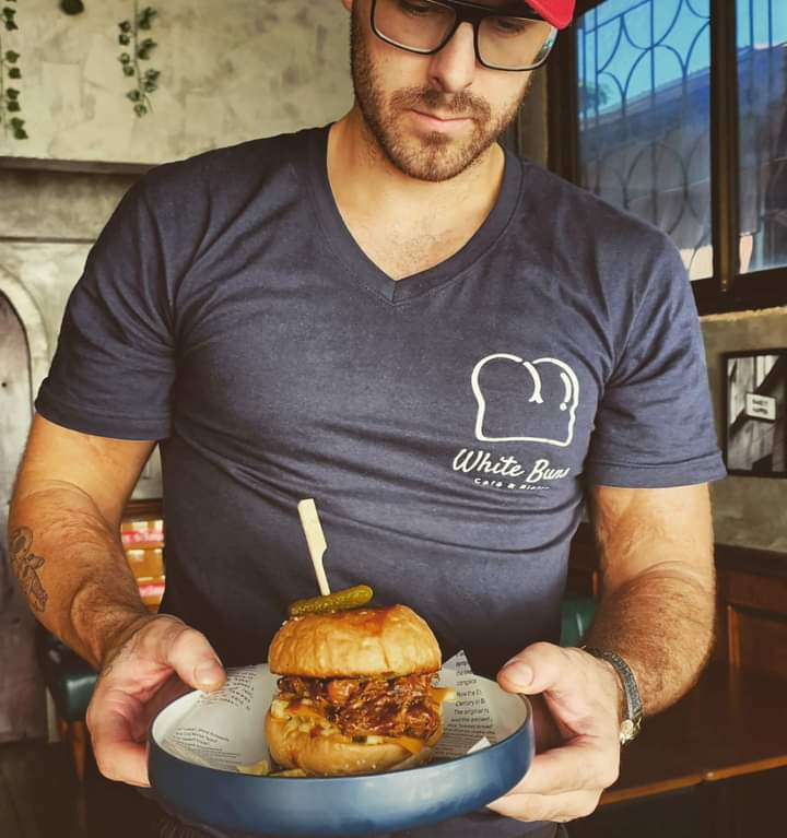 Founder of White Buns Cafe & Bistro presenting a signature burger